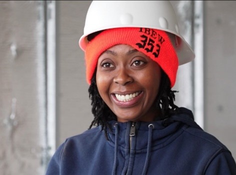 a photo of Stephanie McLean in a white hardhat and neon orange beanie with black text that says, "IBEW 353."